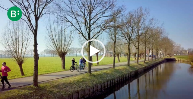 Beeld uit de video: fietsers op een fietspad langs het water en weilanden.